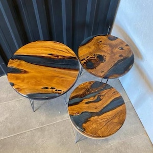 May include: Three round wooden tables with black resin inlays. The tables are different sizes and are on black metal legs.