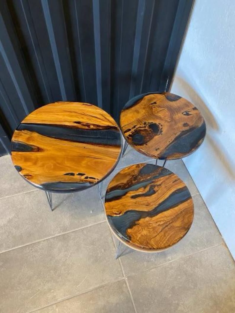 May include: Three round wooden tables with black resin inlays. The tables are different sizes and are on black metal legs.