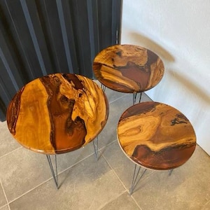 May include: Three round wooden tables with black metal hairpin legs. The tabletops are made of wood with a natural wood grain and a brown, orange, and red epoxy resin finish.