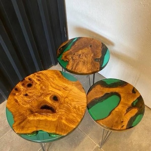May include: Three round wooden tables with green epoxy resin inlays. The tables are different sizes and are arranged in a staggered formation. The tables have black metal hairpin legs.