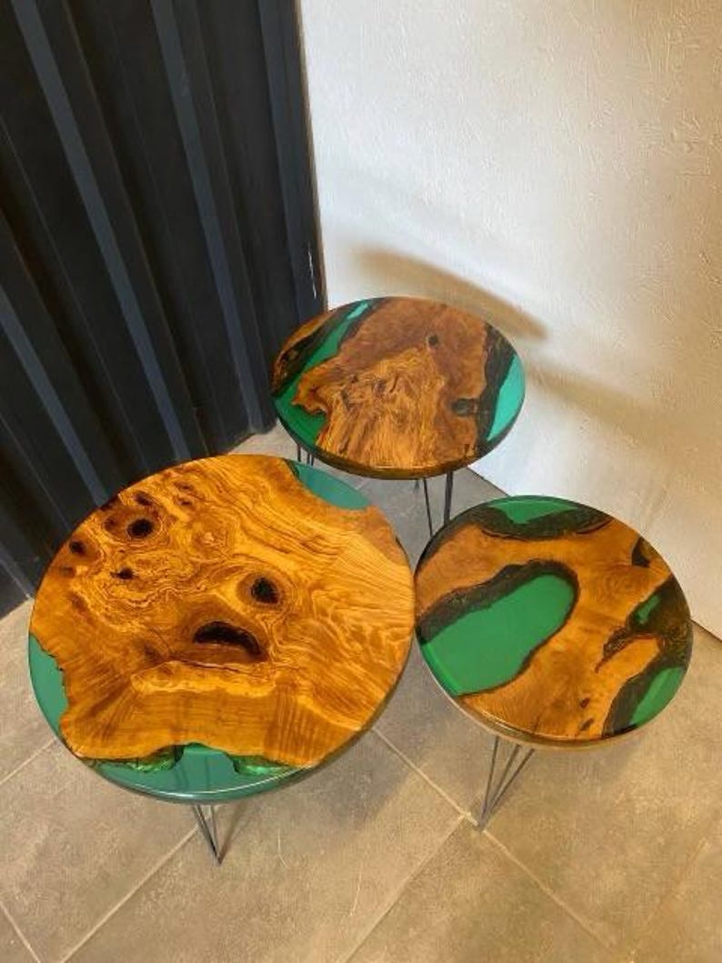 May include: Three round wooden tables with green epoxy resin inlays. The tables are different sizes and are arranged in a staggered formation. The tables have black metal hairpin legs.