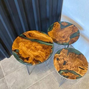 May include: Three round wooden tables with green resin accents. The tables are different sizes and are on black metal hairpin legs.