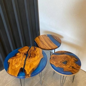 May include: Three round wooden tables with blue epoxy resin tops. The tables are different sizes and are on black metal hairpin legs.