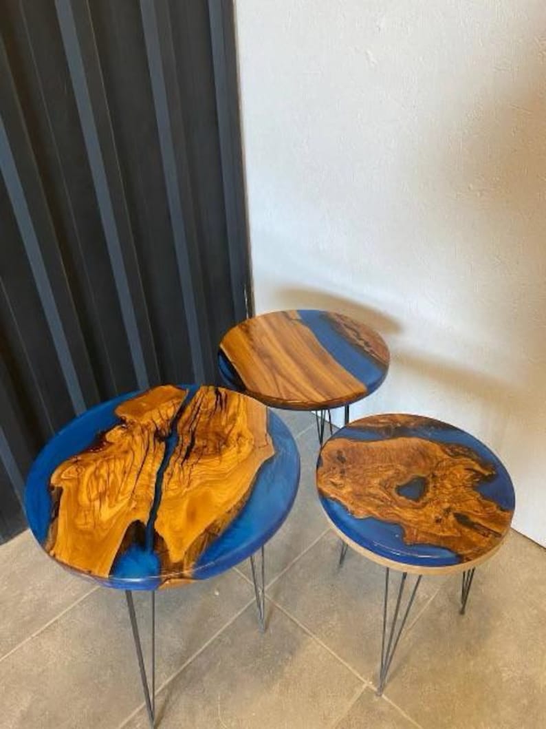 May include: Three round wooden tables with blue epoxy resin tops. The tables are different sizes and are on black metal hairpin legs.