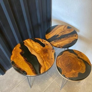 May include: Three round wooden tables with black epoxy resin. The tables have a natural wood grain pattern and are on black metal legs.