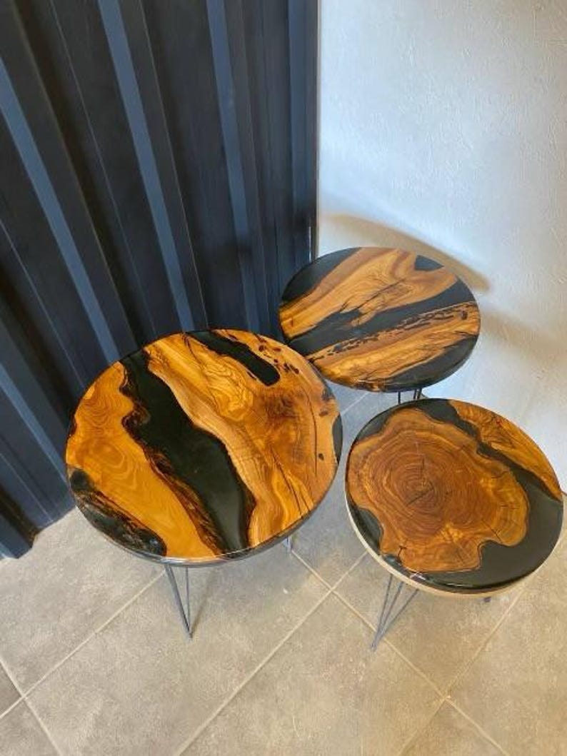 May include: Three round wooden tables with black epoxy resin. The tables have a natural wood grain pattern and are on black metal legs.