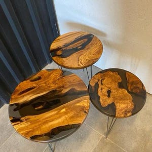 May include: Three round wooden tables with black epoxy resin inlays. The tables are different sizes and are on black metal hairpin legs.