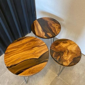 May include: Three round wooden tables with black resin accents and black metal hairpin legs. The tables are arranged in a decreasing size order.