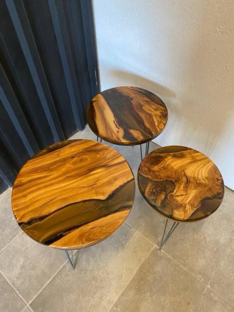 May include: Three round wooden tables with black resin accents and black metal hairpin legs. The tables are arranged in a decreasing size order.