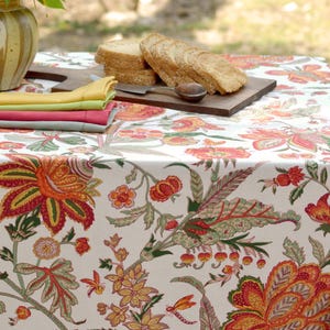 May include: A white tablecloth with a floral pattern in shades of red, orange, green, and yellow. The tablecloth is laid on a table with a wooden cutting board and a stack of sliced bread.