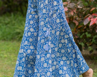May include: Blue palazzo pants with a white floral pattern. The wide-leg pants have a drawstring waist and a tassel detail. The fabric is lightweight and flowing, suitable for warm weather. The pants are worn outdoors on a grassy area.