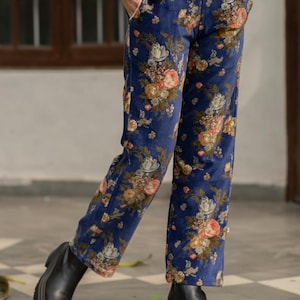 Puede incluir: Pantalón de terciopelo azul con estampado floral. El pantalón tiene un corte ajustado y una pierna recta.