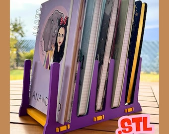 May include: A purple and yellow notebook organizer holding several notebooks. The organizer has a slotted design and the word "ANAND" is visible on one of the notebooks. The notebooks have various covers with illustrations and designs.