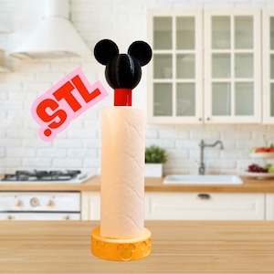 Op de afbeelding: Een gele keukenrolhouder met een Mickey Mouse-hoofd erop. De houder staat op een houten aanrecht in een keuken.