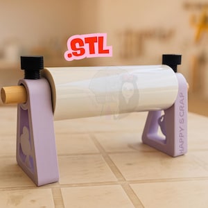 Könnte beinhalten: Ein hellvioletter Bastel-Vinylrollenhalter mit einem Holzdübel und schwarzen Knöpfen. Der Halter hat ein ausgeschnittenes Design und die Worte "HAPPY SCRAP" sind auf der Seite aufgedruckt. Das Wort ".STL" steht in Rosa und Rot über dem Halter.