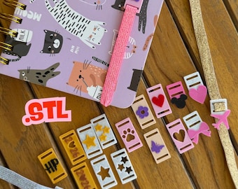 May include: A spiral-bound notebook with a cat pattern, a pink elastic band, and various decorative bookmark charms. Charms include hearts, stars, paw prints, and a butterfly. The word "STL" is also visible.