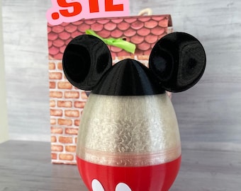 May include: A 3D printed Mickey Mouse egg-shaped container with black ears, a black top, a white middle section, and a red bottom with white circles. The container is sitting on a wooden surface.