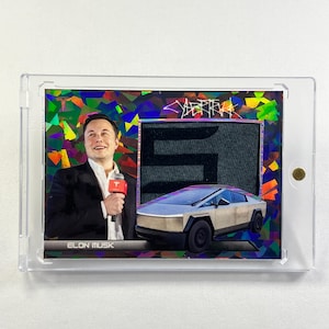 May include: A trading card featuring Elon Musk, the CEO of Tesla and SpaceX, holding a microphone. The card has a colorful background with a black and white image of the Cybertruck in the background. The card also has the text "Cybertruck" and "Elon Musk" printed on it.