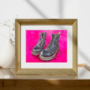 Puede incluir: Una pintura enmarcada de dos botas de cuero negras sobre un fondo rosa brillante. Las botas tienen cordones y están atadas.
