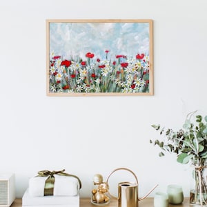 May include: A framed floral painting featuring red poppies and white daisies against a light blue sky. The artwork is in a wooden frame and hangs on a white wall. The painting is a colorful depiction of a flower field.