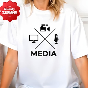 May include: White t-shirt with a black graphic featuring a computer monitor, video camera, and microphone crossed with lines, and the word "MEDIA" below. A red "Quality Designs" sticker is in the upper left corner.