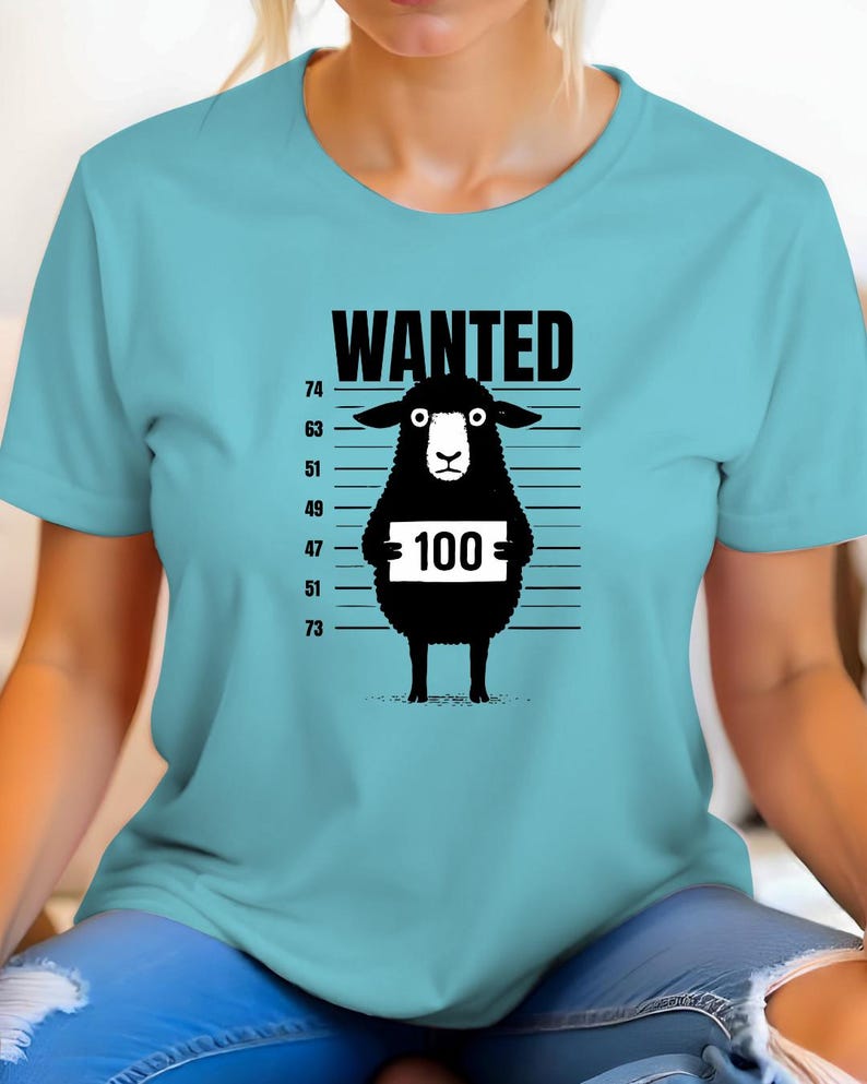 May include: A light blue t-shirt featuring a black sheep illustration with the word "WANTED" above it. The sheep holds a sign with the number "100" on it, against a height chart background.
