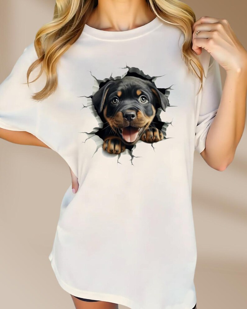May include: White t-shirt with a graphic of a Rottweiler puppy peeking out of a cracked wall.