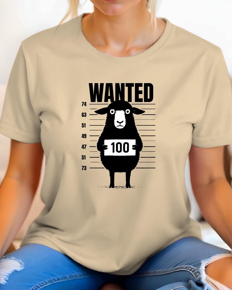 May include: A beige t-shirt featuring a black graphic of a sheep with the word "WANTED" above it. The sheep holds a sign with the number "100" on it, set against a height chart.