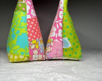 May include: Two colorful, cone-shaped fabric decorations. Each has a patchwork design with various floral and geometric patterns in shades of pink, green, blue, and yellow. The tops are finished with a small loop and bead detail.
