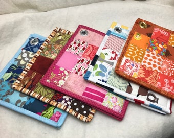 May include: Five colorful patchwork fabric squares with a decorative stitched border. Each square has a different pattern and color scheme, including pink, blue, orange, and brown.