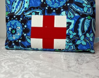 May include: A rectangular zippered pouch with a blue floral pattern and a red and white cross design. The pouch features a silver zipper and a small loop on one side. The floral pattern includes shades of blue, black, and green.