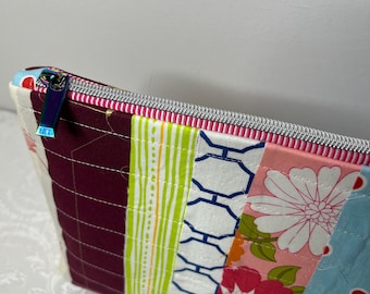 May include: A colorful patchwork zippered pouch with a rainbow zipper pull. The pouch features vertical panels of various patterned fabrics, including floral, geometric, and striped designs. The pouch is likely used for cosmetics or small items.