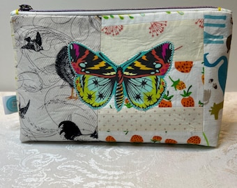 May include: A rectangular, patchwork fabric pouch with a zipper closure. The pouch features a large, colorful butterfly applique. The patchwork includes patterns of birds, strawberries, and other designs. The zipper is purple.