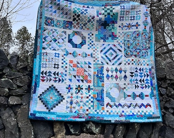May include: A large quilt made of various blue, white, and red fabric squares. The quilt is hanging on a stone wall.