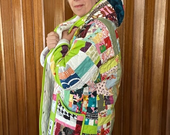 May include: A long, green quilted jacket with a hood. The jacket is made of patchwork fabric in various colors and patterns. The jacket has a large pocket on the left side.