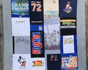 May include: A gray quilt made from various t-shirts with different city and location names, including Grand Cayman, Yellowstone, Key West, London, Paris, Hollywood, New York, and Cozumel. The quilt also features a Mickey Mouse design.