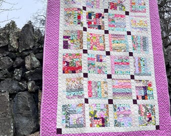 May include: A pink and white patchwork quilt with a variety of floral and geometric patterns. The quilt is quilted with a small circle pattern and has a pink border.
