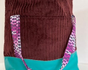 May include: A brown corduroy tote bag with a teal bottom and a pink and purple patterned strap.
