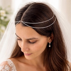 May include: A silver-toned headpiece featuring a delicate chain design that rests across the forehead and wraps around the crown of the head. The accessory consists of a central vertical chain connected to two horizontal strands that drape elegantly.
