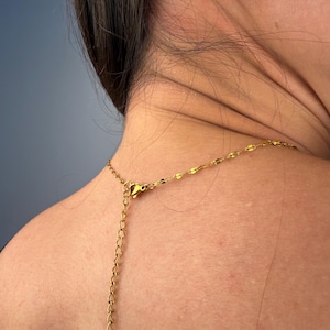 May include: A gold-toned necklace featuring a delicate chain with flat, reflective, oval-shaped links. The necklace includes a thin extender chain with a lobster claw clasp, allowing for adjustable length around the neck area.