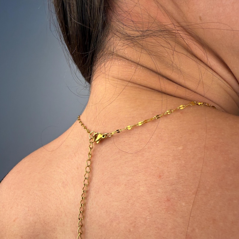 May include: A gold-toned necklace featuring a delicate chain with flat, reflective, oval-shaped links. The necklace includes a thin extender chain with a lobster claw clasp, allowing for adjustable length around the neck area.