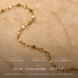 May include: A gold-toned chain necklace featuring elongated, flattened oval links. Text on the image specifies: WATERPROOF, TARNISH FREE, SKIN SAFE, and a size of 35 cm + 6 cm extender / 13.8" + 2.4". The text also includes a note about size adjustments.