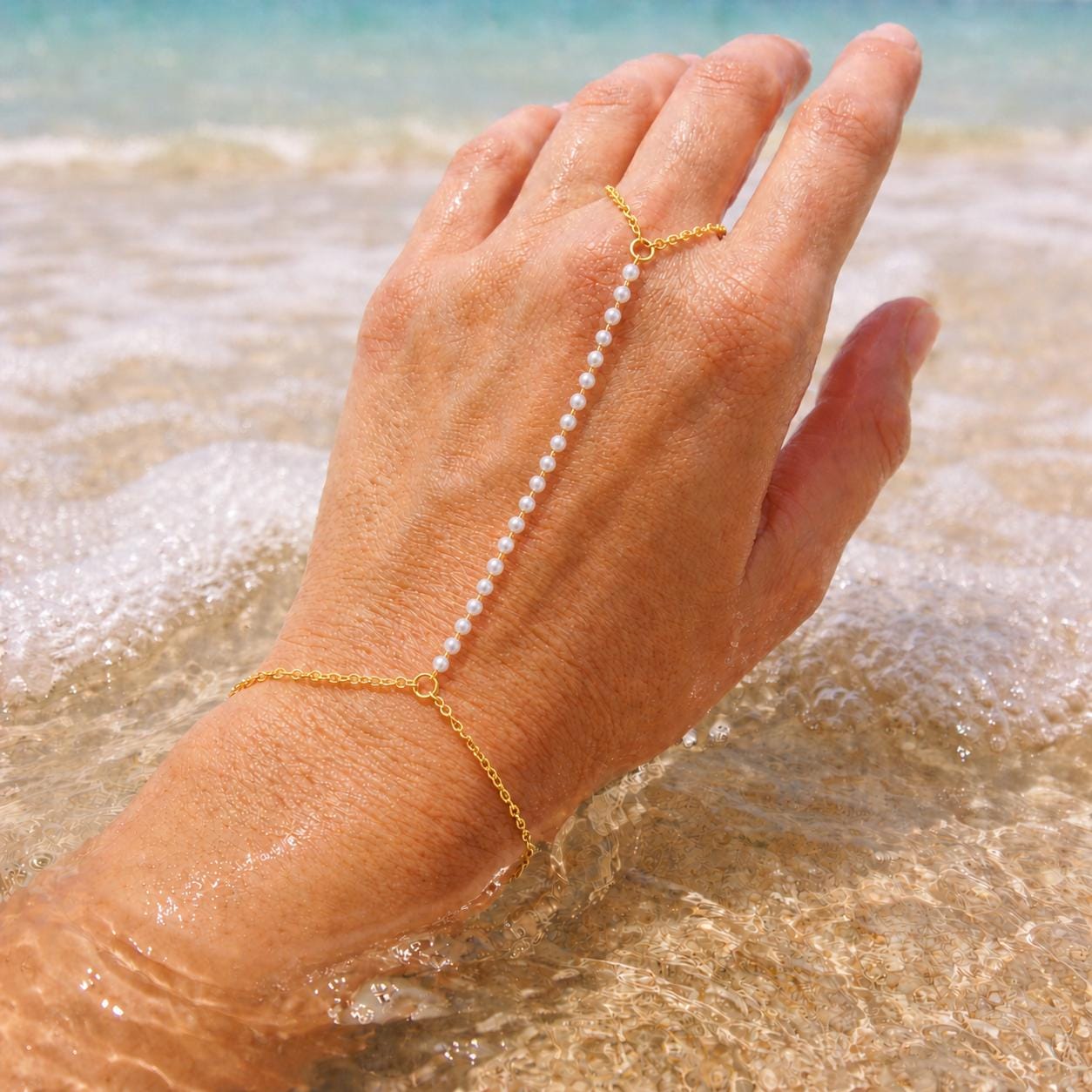 Gold-tone stainless steel pearl hand chain draped across wrist for elegant bridal hand jewelry