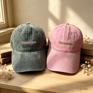 Può includere: Due cappellini da baseball con finitura slavata. Il cappellino a sinistra è grigio antracite con la scritta "Süssmaus" ricamata in rosa chiaro. Il cappellino a destra è rosa polvere con la scritta "Süssmaus" ricamata in verde scuro. Visiera curva.