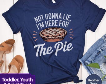 May include: A navy blue t-shirt with the text "NOT GONNA LIE, I'M HERE FOR THE PIE" and a graphic of a pie. The text is in white and the pie is brown with a white crust.