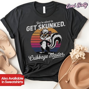 Può includere: T-shirt nera con un disegno di puzzola con occhiali da sole, con la scritta "You're about to GET SKUNKED." e "Cribbage Master." Il design include una grafica del tramonto. Disponibile anche in felpe.