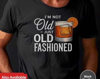 Puede incluir: Una camiseta negra con el texto "I'm not Old - Just Old Fashioned" en blanco. El texto está acompañado por un gráfico de un vaso de whisky con una rodaja de naranja.