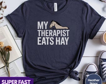 May include: A navy blue t-shirt with a white graphic of a horse and the text "My Therapist Eats Hay".