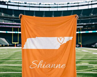 May include: Orange fleece blanket with a white outline of the state of Tennessee and a heart in the center. The name "Shianne" is written in white cursive at the bottom.