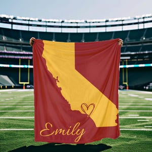 May include: A red and gold fleece blanket with the outline of the state of California and a heart. The name "Emily" is written in gold script on the blanket.